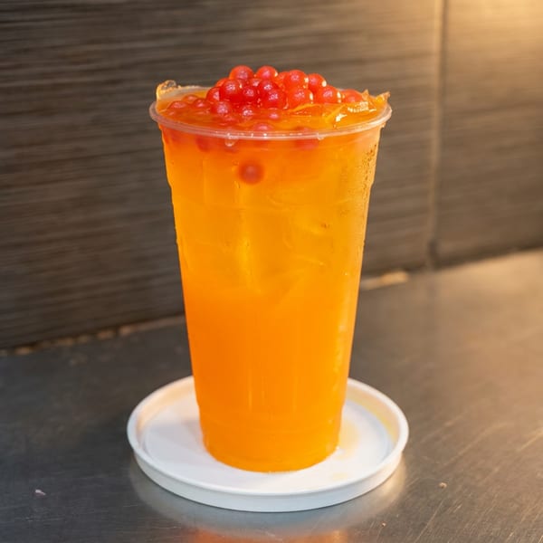 Bright orange iced drink topped with red fruit pearls and citrus slices, served in a clear cup on a white saucer.