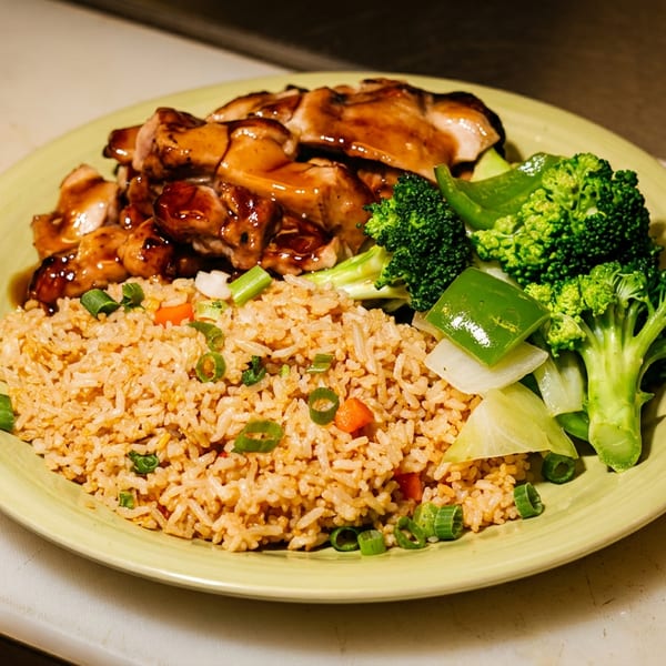 Plate of glazed chicken with fried rice, broccoli, bell peppers, onions, and green onions.